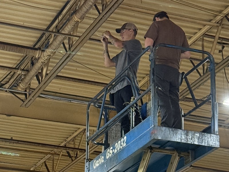 Michigan Security Systems technicians running overhead paging and speaker cabling from a scissor lift in a commercial industrial facility