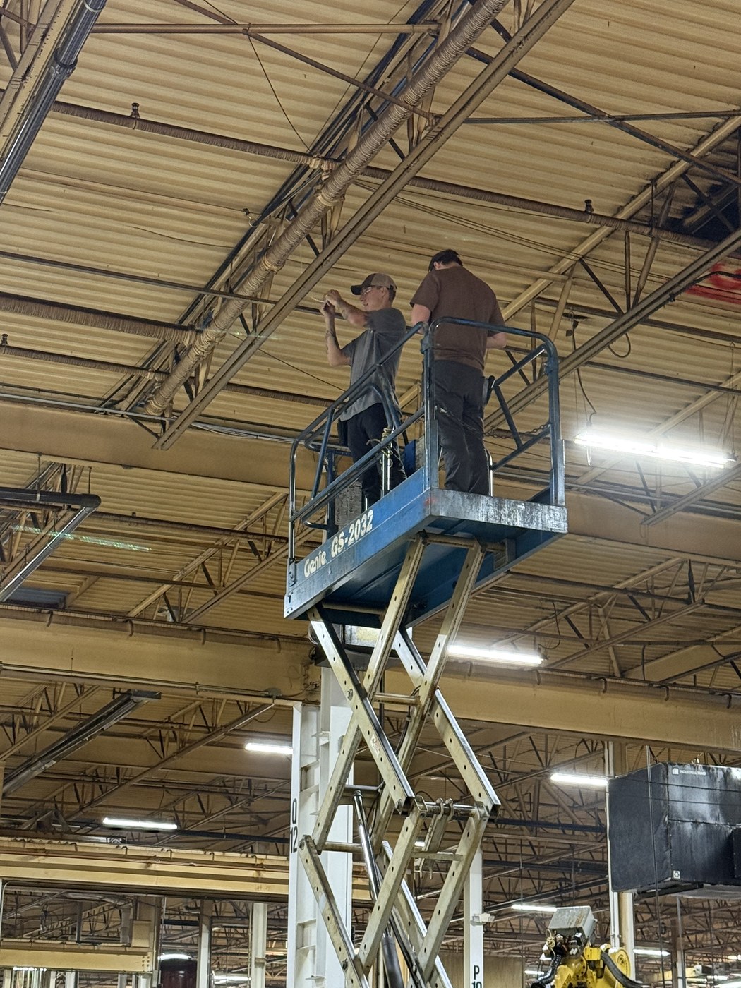 Technicians on a scissor lift installing ceiling security equipment at a manufacturing facility